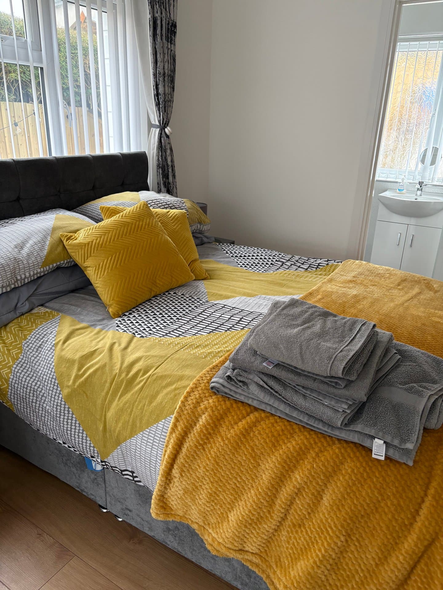 Comfortable bedroom featuring a stylish black upholstered bed, vibrant yellow and grey bedding, and en-suite bathroom access. Bright and airy space with garden views.